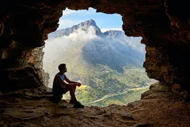 A man looking out into a valley from a cave opening.