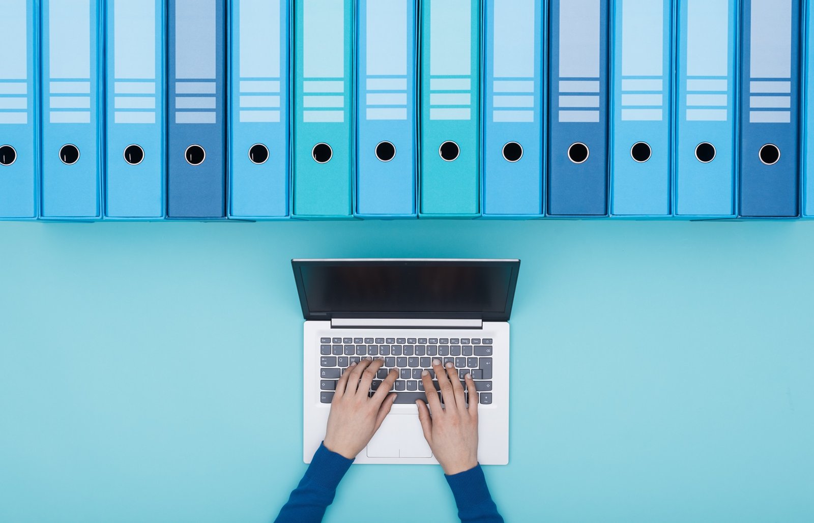 a person typing on a laptop searching for archived files in ring binders